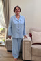 Elderly woman wearing a light blue linen pyjama set with elastic-waist pants and a comfortable button-up jacket for seniors.