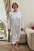 Elderly woman wearing a white geriatric pyjama with long sleeves, designed for seniors to provide comfort and ease of dressing.